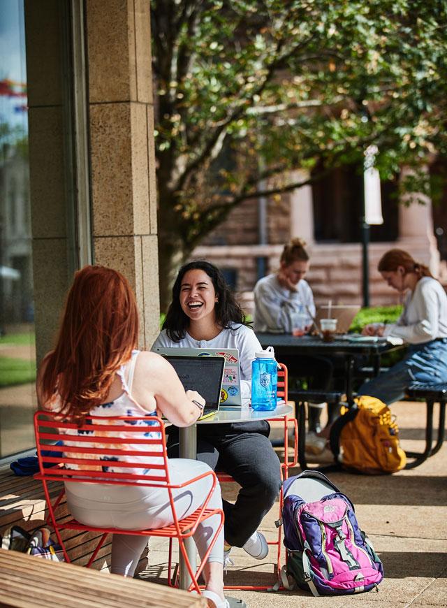 学生们坐在图书馆外的桌子旁，边学习边谈笑风生